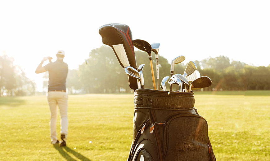 Man playing golf on course with golf bag full of clubs